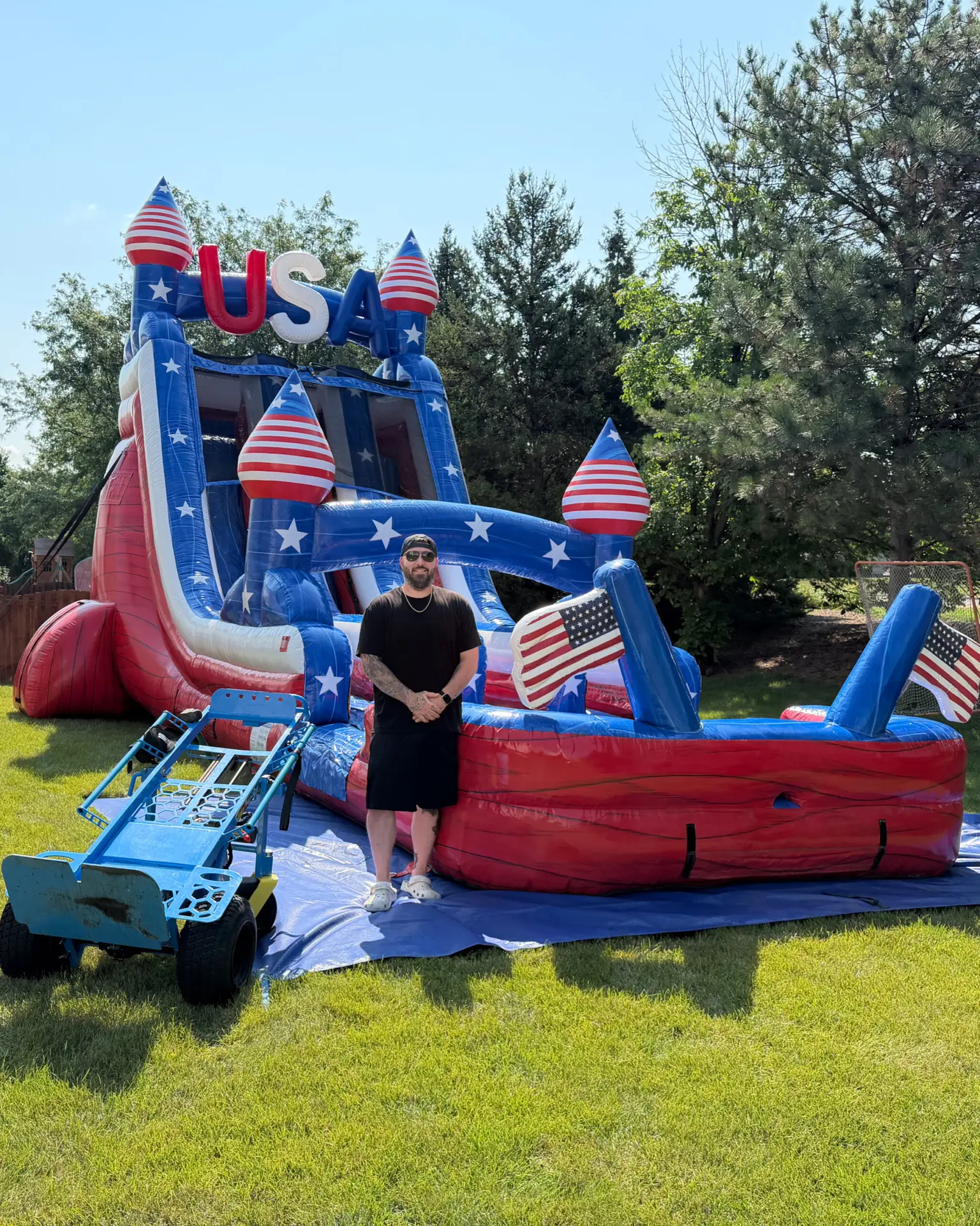 Josh, owner of Best Bounce Party Rentals, standing in front of a USA-themed inflatable water slide in Tinley Park, Illinois.